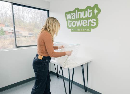 A woman is setting up a table in a room with a sign at Walnut Towers at Frick Park, Pittsburgh, 15217