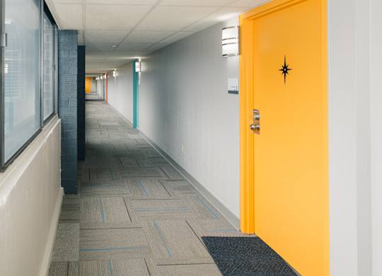 A hallway with a yellow door and a black doorknob at Walnut Towers at Frick Park, Pittsburgh