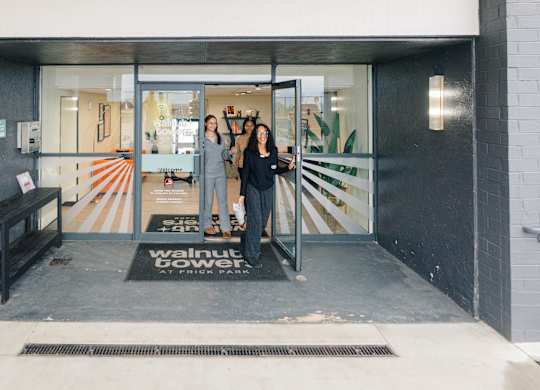 Two women standing in front of a glass door with a sign that says at Walnut Towers at Frick Park, Pittsburgh, PA 15217