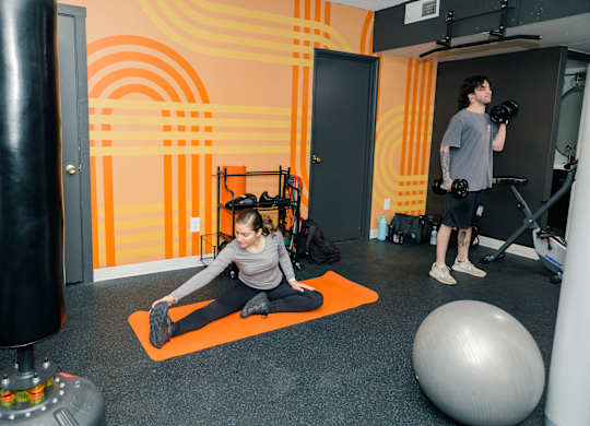 A man and a woman are exercising in a gym with orange and black accents at Walnut Towers at Frick Park, Pittsburgh