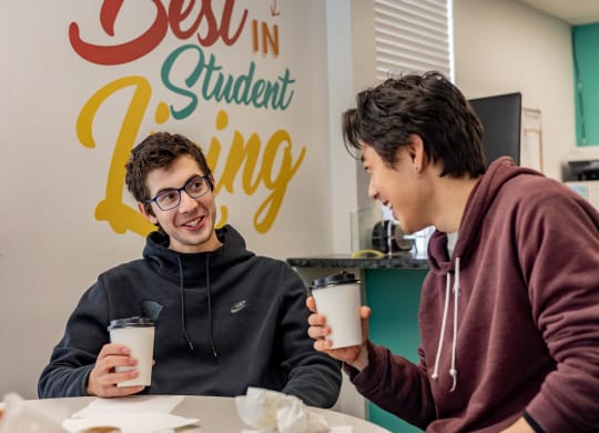 two students sitting at a table in front of a sign that says best in student living at University Commons Apartments, Oakland, Pittsburgh