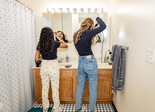 two women doing their hair in a bathroom at University Commons Apartments, Oakland, Pittsburgh