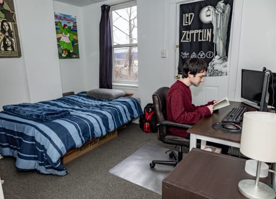 a student sits at a desk in a dorm room with a bed in the background at University Commons Apartments, Oakland, Pittsburgh