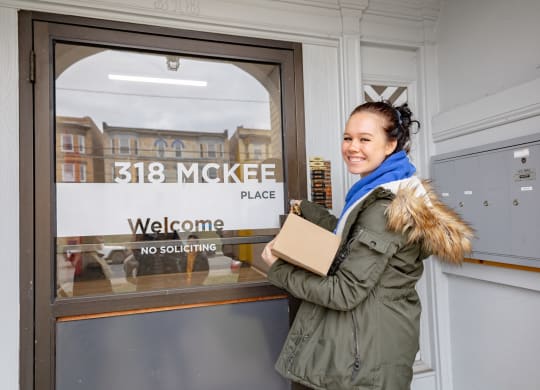a woman standing in front of a door with a cardboard box in her hand at University Commons Apartments, Oakland, Pittsburgh