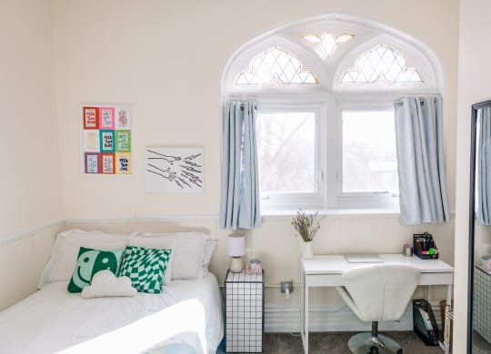 a bedroom with a white bed with green and white pillows and a white desk at University Commons Apartments, Oakland, Pittsburgh