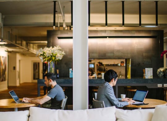 two men sitting at tables working on their laptops in a large open space at Bakery Living in Pittsburgh, PA 15206