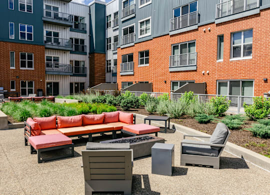 A patio with a red couch, grey armchair, and a grey table.