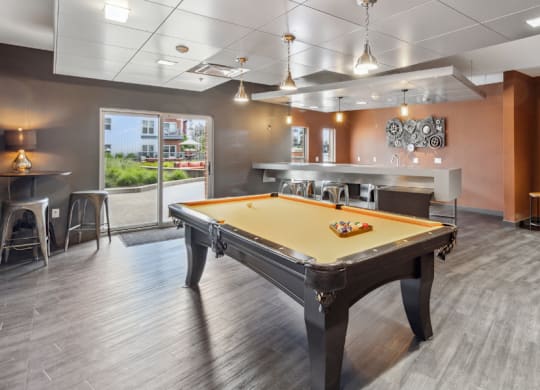 A pool table is in the middle of a room with a couch and a bar area.