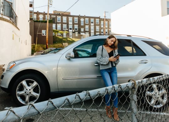 a woman leaning against a car looking at her phone at University Commons Apartments, Oakland, Pittsburgh
