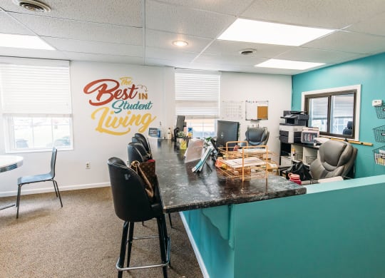 a desk with chairs and a counter in front of a wall with a sign that says best at University Commons Apartments, Oakland, Pittsburgh
