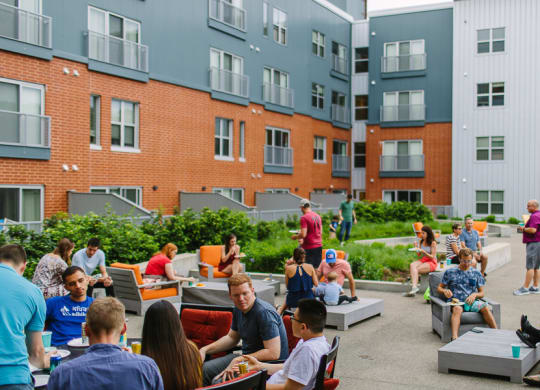 a group of people sitting and standing on a patio in front of an apartment building