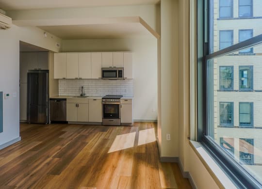 an empty living room with a large window and a kitchen at The Commonwealth Building, Pittsburgh, 15222