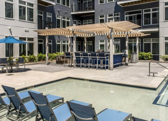 a pool with blue lounge chairs and umbrellas in front of an apartment building
