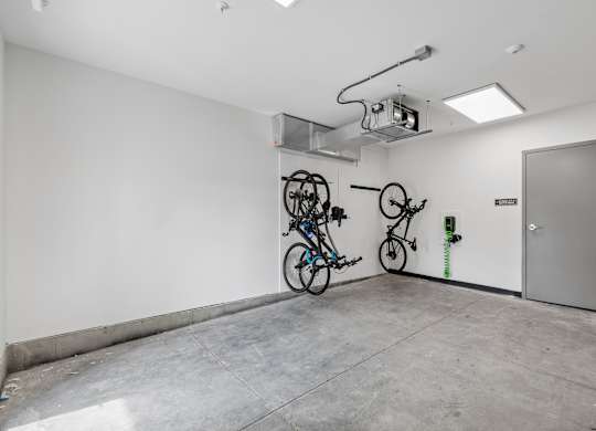 A room with a white wall and a grey door has a bicycle hanging on the wall.