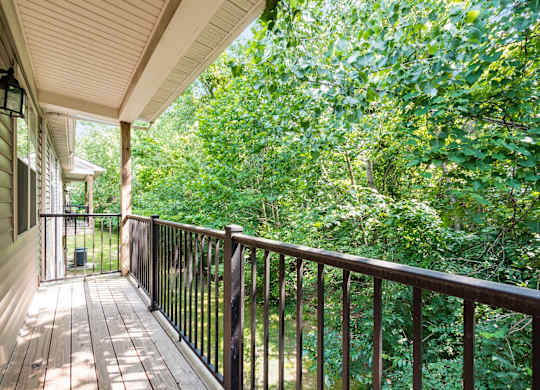 A wooden deck with a railing overlooks a lush green forest. at River View at Bexley Apartments, River View at Bexley, Ohio