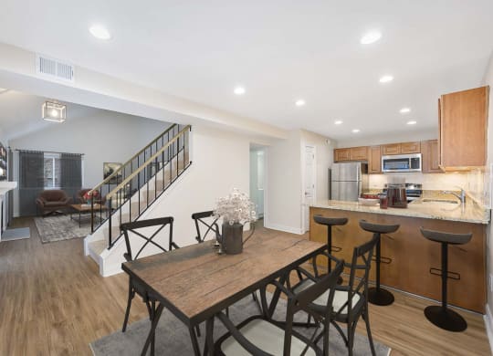 a dining area with a wooden table and chairs and a kitchen with a staircase in the background at Harpers Point Apartments, Cincinnati, Ohio