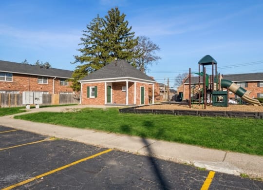 a playground sits in the middle of a grassy area in front of a brick building