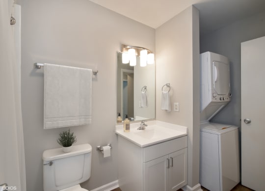a bathroom with a toilet sink mirror and a washer and dryer at 7 Pointe Apartments, Indianapolis, 46205