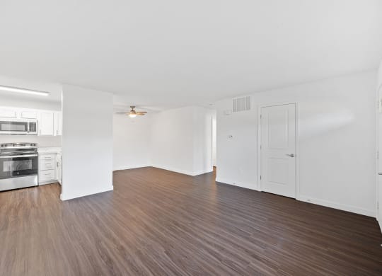 the living room and kitchen of an apartment with wood flooring and white walls