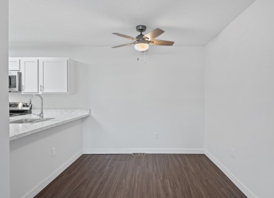 an empty living room with a ceiling fan and a kitchen