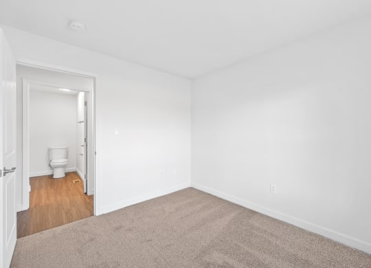 a bedroom with white walls and carpet and a bathroom with a toilet