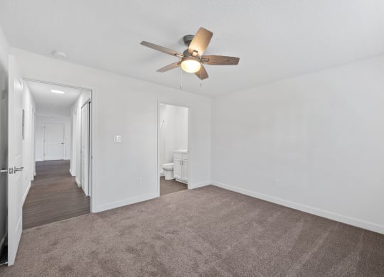 an empty living room with a ceiling fan and a hallway