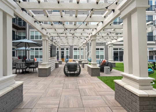 a pergola with a seating area and a lawn in front of an apartment building