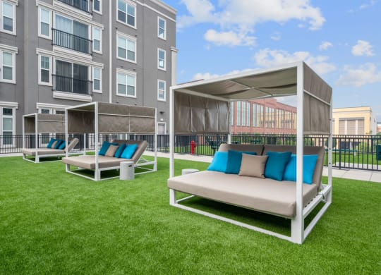a patio with couches and chairs on a lawn in front of an apartment building
