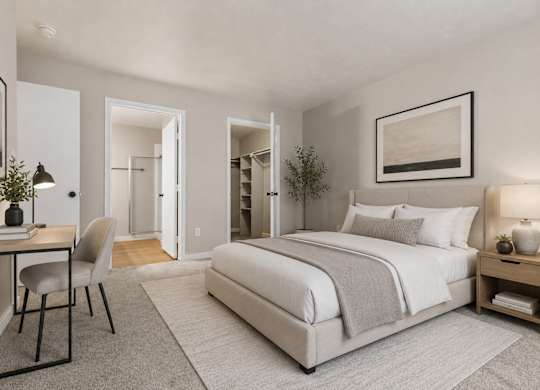 A bedroom with a large bed, a desk with a chair, and a nightstand with a lamp.