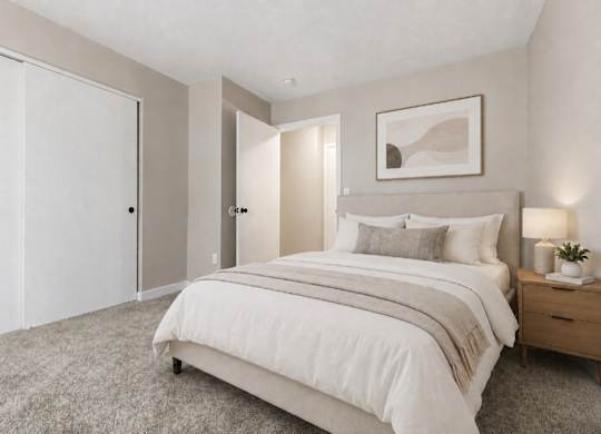 A bedroom with a large bed and a nightstand with a plant on it.