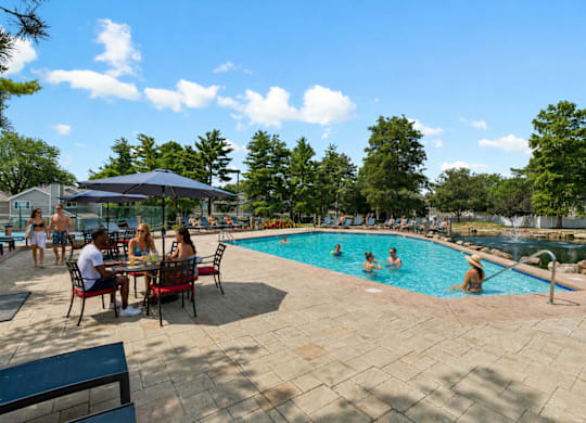 A group of people are sitting at a table by a pool.