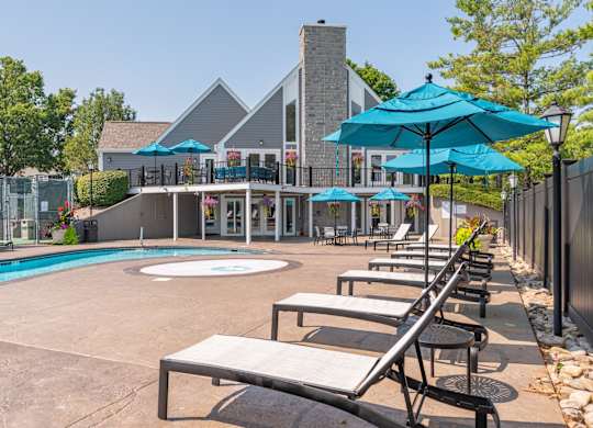 A pool area with lounge chairs and umbrellas in front of a house.
