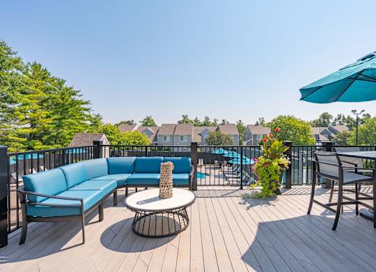 A blue sofa and a table with a vase of flowers are on a wooden deck.
