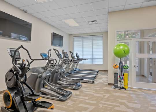 A gym with treadmills, exercise bikes, and a television.