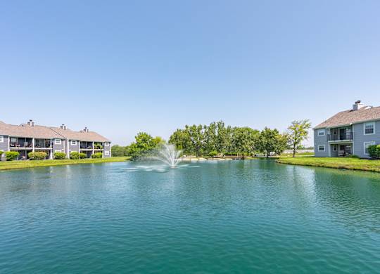 A fountain in the middle of a lake surrounded by houses.