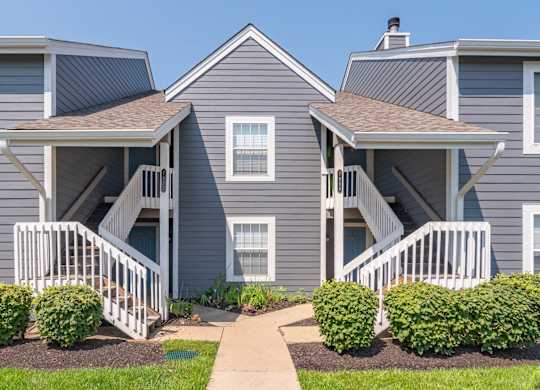 A grey house with a white porch and a brown roof.