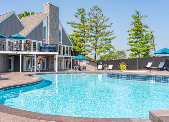 A large swimming pool in front of a house with a deck and lounge chairs.
