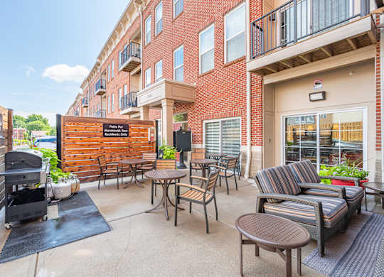 A patio with a grill and chairs is surrounded by a brick building.