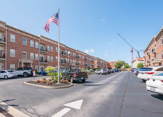 A street view with a flag on a pole and cars parked on the side.