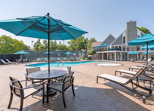 A poolside area with a table and chairs under a blue umbrella.