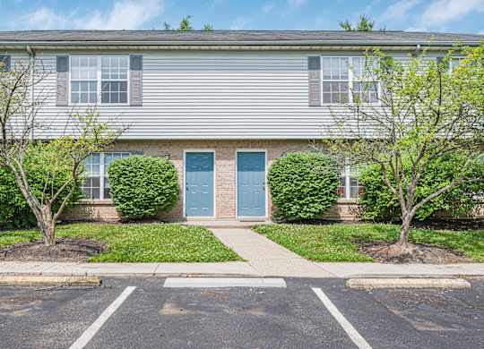 A grey building with a blue door and two trees in front.