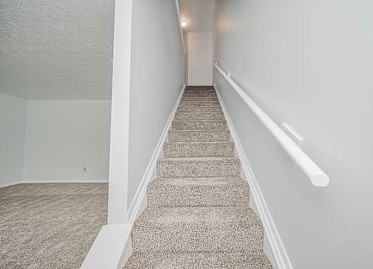 A staircase with a carpeted runner and white handrails.