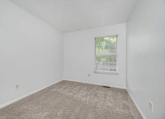 A room with a carpeted floor and a window with blinds.