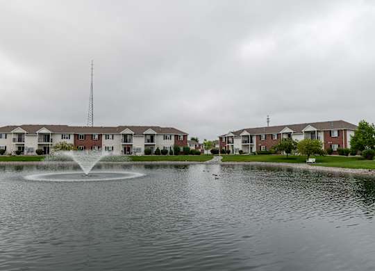 a fountain in the middle of a pond with houses in the background