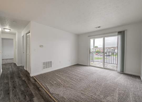 an empty living room with a sliding glass door to a balcony