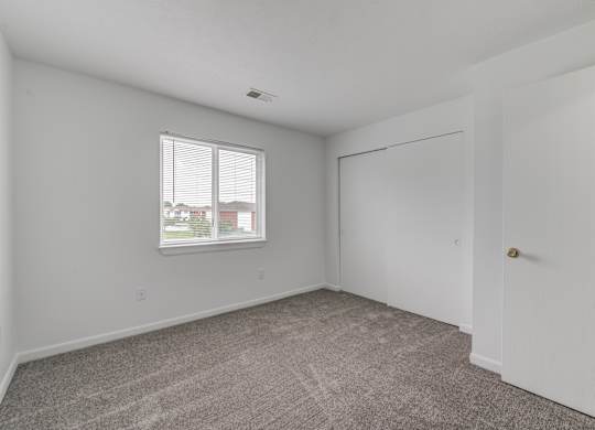 the living room of an apartment with carpet and a window