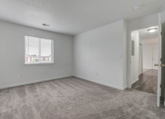 the living room of an apartment with carpet and a window