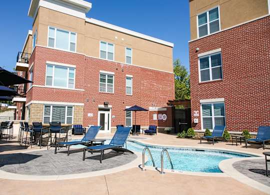 A pool area with lounge chairs and umbrellas in front of a brick building.