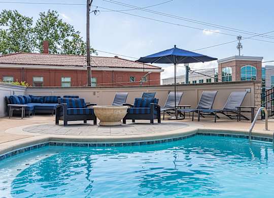 A pool with a blue umbrella and chairs.