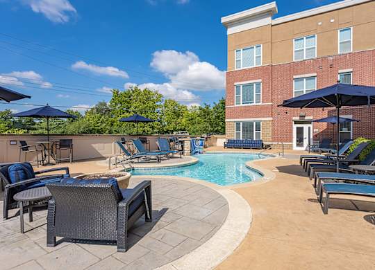 A pool surrounded by chairs and umbrellas with a building in the background.